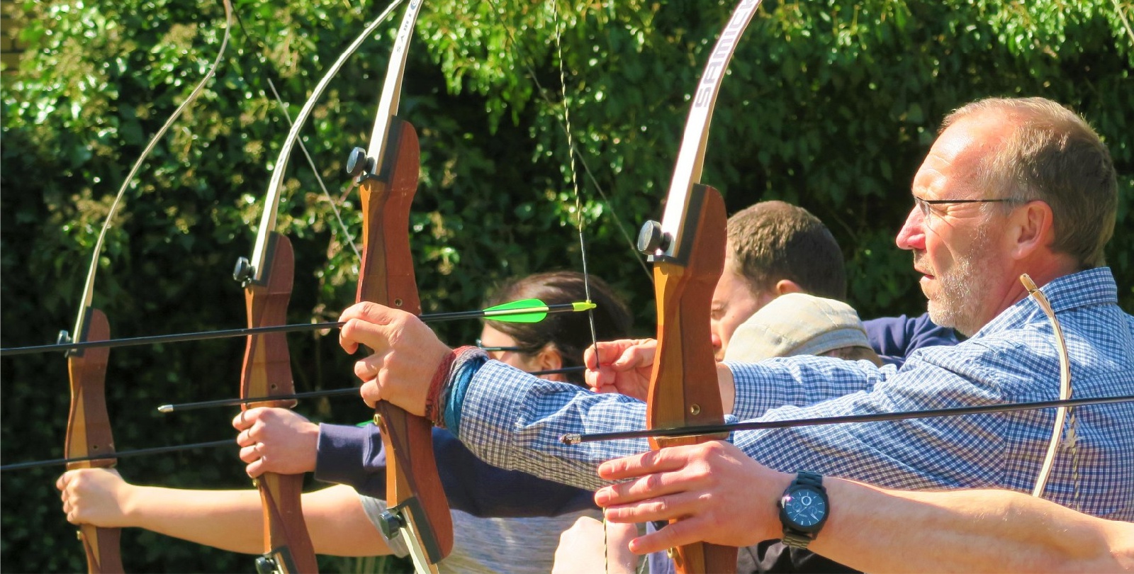 Eine Gruppe steht lachend um eine farbige Zielscheibe zum Bogenschie�en in der einige Pfeile stecken